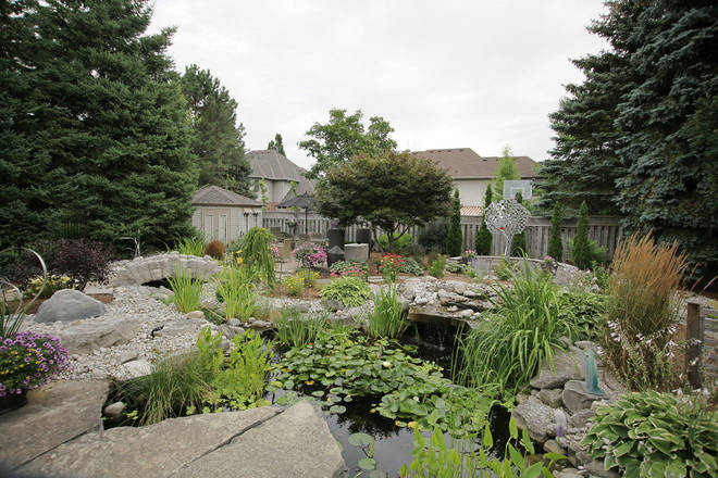 Custom hand-hewn stone bridge, stone landscape, and round hand-hewn stone retaining wall around metal garden tree sculpture.