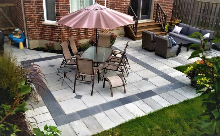 Banas dove gray square cut flag stone with coda black border and inlays. Custom patio installation in London, Ontario.